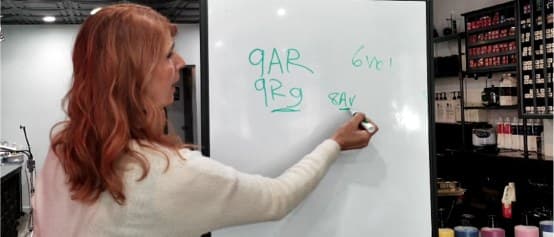A Healthy Color educator teaching color formulation on a whiteboard in the salon.